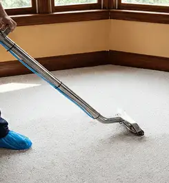 Steam carpet cleaning technician using a hot-water extraction wand on a residential carpet, wearing blue protective shoe covers Chicago, IL.