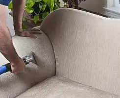 Professional upholstery cleaner deep-cleaning a fabric sofa with a handheld extraction tool and hose in Chicago, IL.